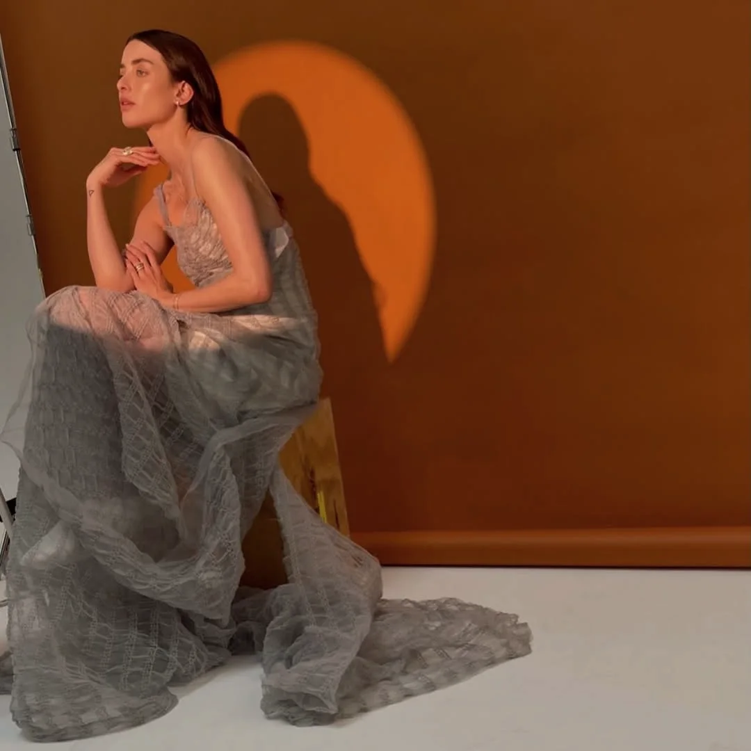 Grey tulle gown in a circle of light against a terracotta wall